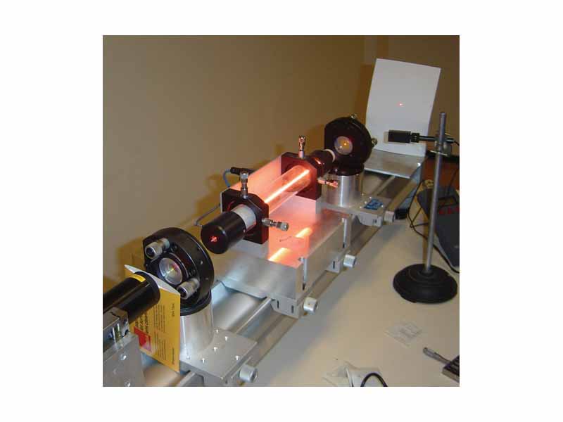 A helium-neon laser demonstration at the Kastler-Brossel Laboratory at Univ. Paris 6. The glowing ray in the middle is an electric discharge producing light in much the same way as a neon light. It is the gain medium through which the laser passes, not the laser beam itself, which is visible there. The laser beam crosses the air and marks a red point on the screen to the right.